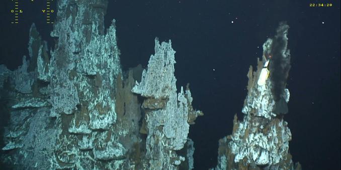 Underwater photo of a deep sea hydrothermal vent - a formation of rugged rocky spikes in dark water. Photo by Ifremer.