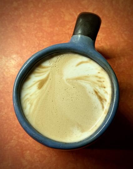 Heavy blue/brown/black ceramic mug on a 70’s orange formica countertop with freshly steamed milk inside that’s have a double shot of espresso pulled on top. The pattern of the espresso is more smooth and flowing that previous ones, it could be an exotic bird looking back at us over its luxurious shoulder of flowing feathers. Or a fire hydrant has let loose up the street and the Summer’s dust and worries are swirling past our feet.