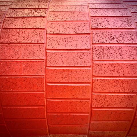 Red-painted bricks stack in a fashion similar to an old rolodex in the shade of a sunny day.