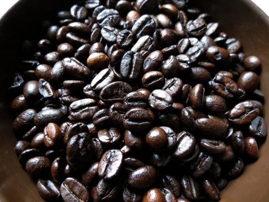 A macro photograph of very dark roasted coffee beans in a bowl.