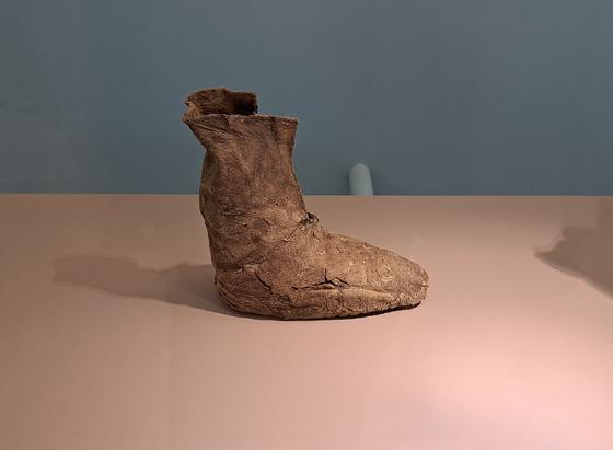A single leather boot with a high ankle, displayed on a flat surface against a plain background. The boot appears old and worn, with visible cracks and creases in the material.