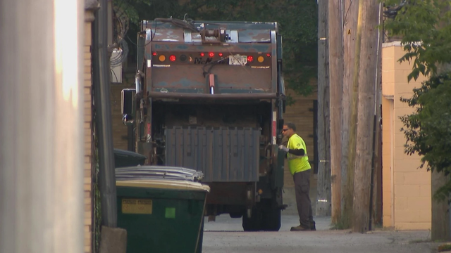 A man in a green shirt stands beside a garbage truck in a Chicago alley.