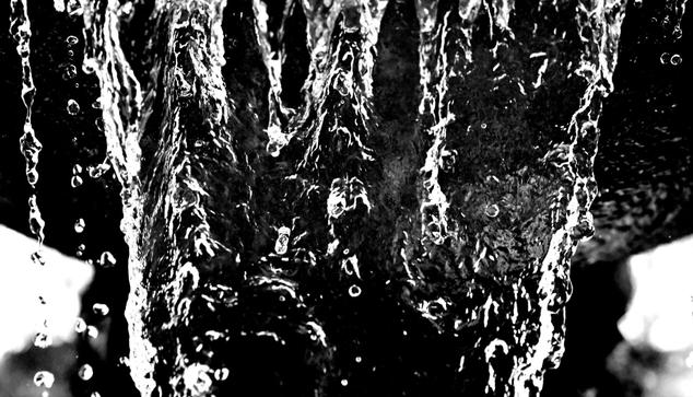 Black and white photo of a fountain taken with a fast shutter speed to show the sheets and droplets of water frozen as they fall.