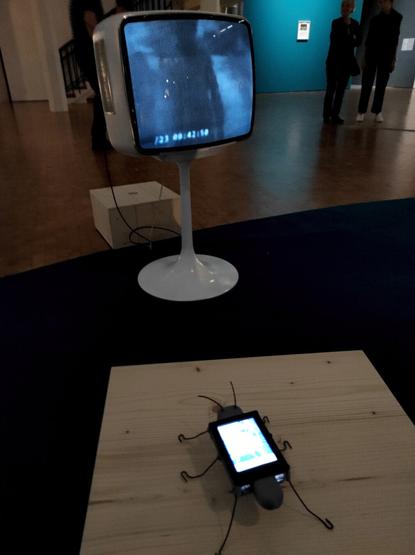 Le cafard digital (DigitalBug) regarde de la vidéo sur un téléviseur des années 70, dans l'espace d'exposition sombre.