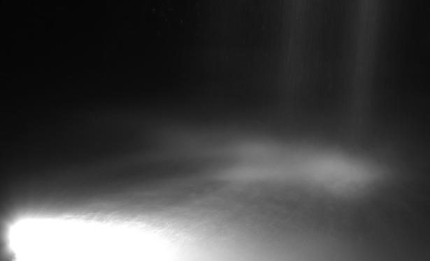 Long exposure photo of a waterfall at night. A light in the water illuminates the water churn.