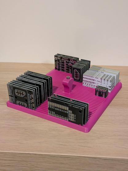 A photo of a 3D printed organiser for small circuit boards. It's a flat rectangular thing with long 2mm wide slots cut into it, and a curved handle sticking up from the middle. There's an array of different sized circuit boards sticking up in neat rows.