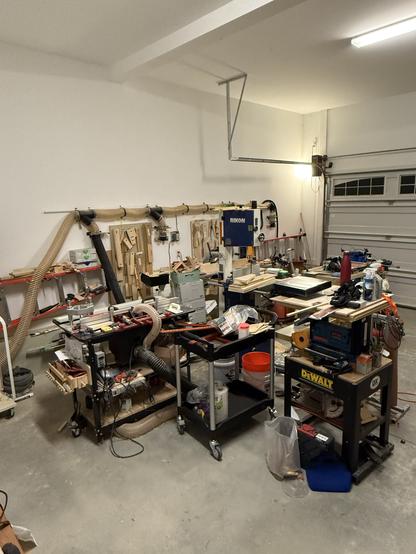 A busy garage workshop filled with various woodworking tools, equipment, and materials. The space is organized but cluttered, conveying a sense of active creativity.