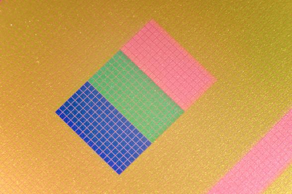 Three rectangles next to each other, one is blue, the other pale green and the third is pink. They rest on a yellow-sand coloured grid with an interesting texture. A pink bar enters the image in the bottom right corner