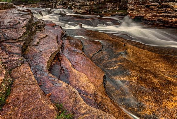 A muli-tiered slab of rock creates a staircase within which a shallow stream cascades down creating a small waterfall.
