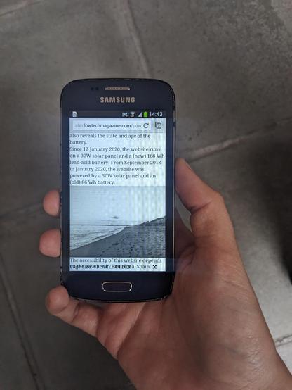 a hand holds an old smartphone with a page of lowtechmagazine.com featuring a dithered image of a beach