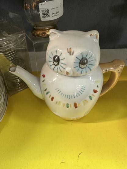 A white ceramic teapot in the shape of an owl. He looks slightly surprised