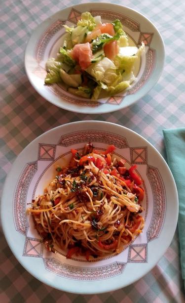 En un plato hondo unos fideos chinos salteados con camarones, pimiento rojo, cebolleta, perejil, cebollino, ajo y salsa laogamma con cacahuetes.
Otro plato hondo con una ensalada de lechuga, pepino y tomate.