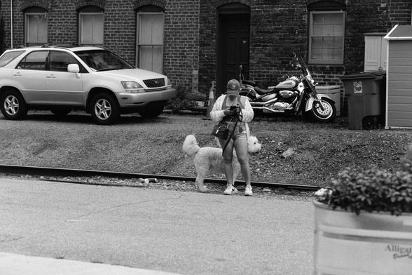 A woman and her very fluffy poodle, she is stopped by the train tracks to look at her phone.  She is wearing a Red Sox hat (nobody’s perfect). A motorcycle is parked in the background.  

Nikon F100 | Nikon 85mm 1.4 | Kentmere 200 200 @ 800, +2 dev

Home developed in XTOL Stock | 10:45 @ 24C