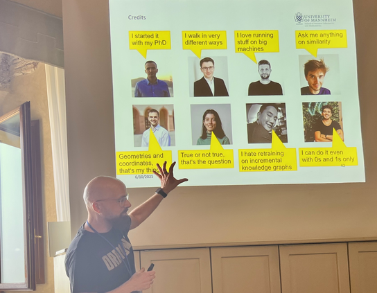 Heiko Paulheil in front of the presentation screen projection, which is listing 8 people and their individual contribution to the RDF2vec project.