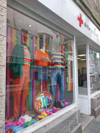 Window of British Red Cross shop displaying clothes in Rainbow colours.