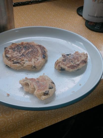 One Welsh cake and two half-eaten pieces on a white plate.