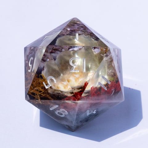 A oversized D20 with a diorama featuring moss, red flowers and a pearly white seashell. Inked in silver.