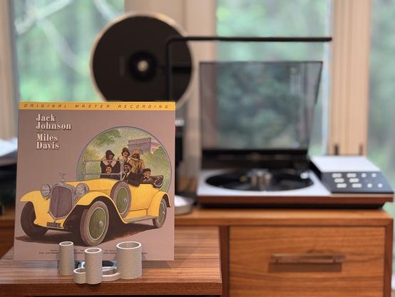 Miles Davis - Jack Johnson LP cover.

A drawing of an old car, painted yellow, with a group of people in it, dressed to go out.

The black LP plays on a vintage, restored Bang & Olufsen Beogram 8002 linear-tracking turntable to the right.