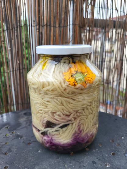 A large mason jar full of yarn. The yarn is coloured a little pink at the bottom and flowers, bark and leaves can be seen between the layers of yarn. The jar is filled to the top.