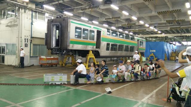 Auto-generated description: A small group of people, including children, ride on a miniature train in an indoor facility with a full-sized train in the background.