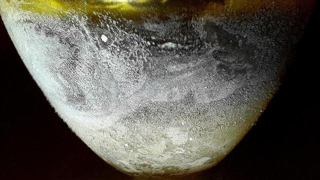 Ice condensing on a  yellow glass tumbler with ice frozen into the bottom, and subzero Jägermeißter foating on top of the water ice sea floor, resembles an ice moon.