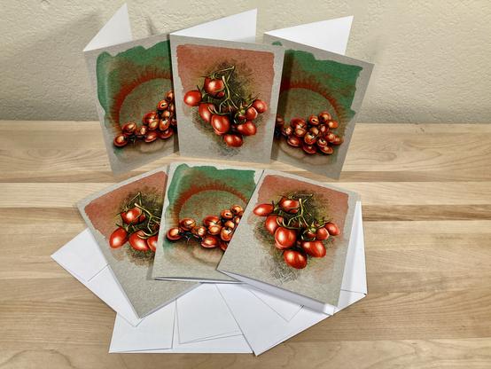 Photograph of a set of six illustrated greeting cards featuring grape tomatoes, arranged around white envelopes on a wooden plank.