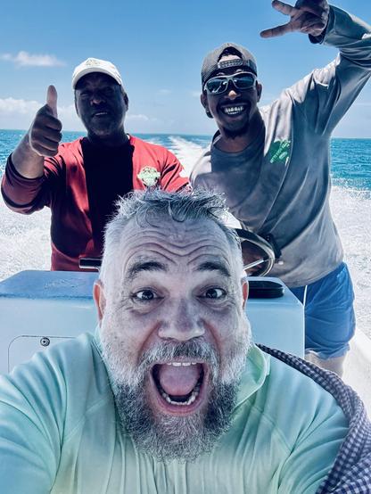 Me, open-mouth grin with the captain and our snorkle guide smiling and waving behind me. The blue sea with the wake of the boat is in the background.