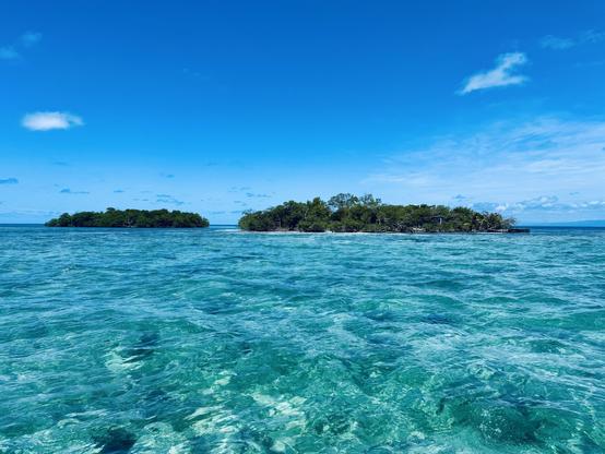 Two small islands—Bread & Butter Cayes—on the horizon. A beautiful shallow ocean and bright blue sky with wispy clouds above.