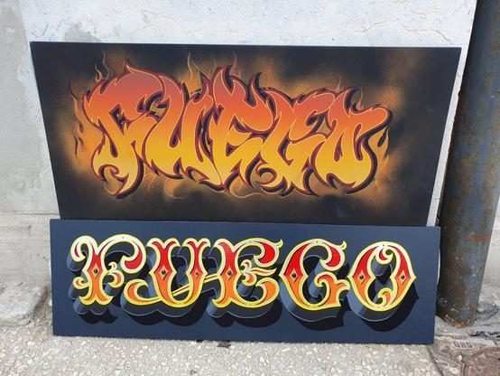 Two signs on black backgrounds both painted with the word fuego in orange and yellow, one in graffiti wildstyle, the other in fairground tuscan lettering
