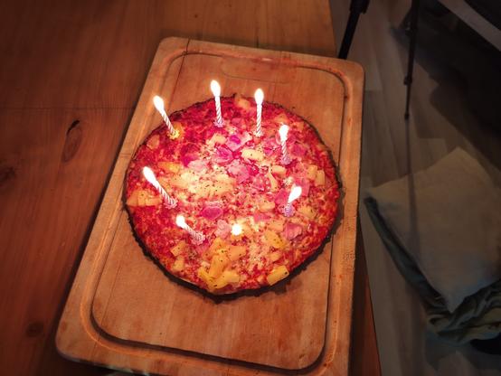 eine Pizza mit 8 Geburtstagskerzen auf einem Holzbrett.