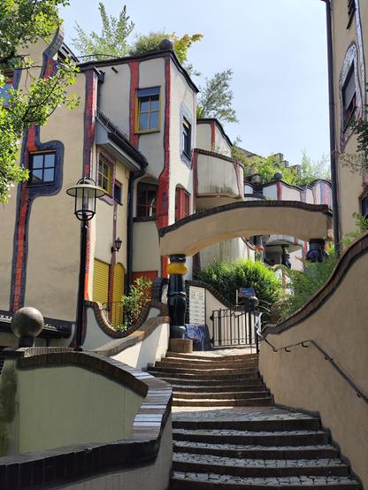 Der Hintereingang oder Haupteingang des Hunderwasserhauses in Plochingen mit einem Bogen. Die Fassaden sind verspielty beige, rote Streifen unterschiedliche Fensteranordnung. Siehe andere Bildbeschreibungen.