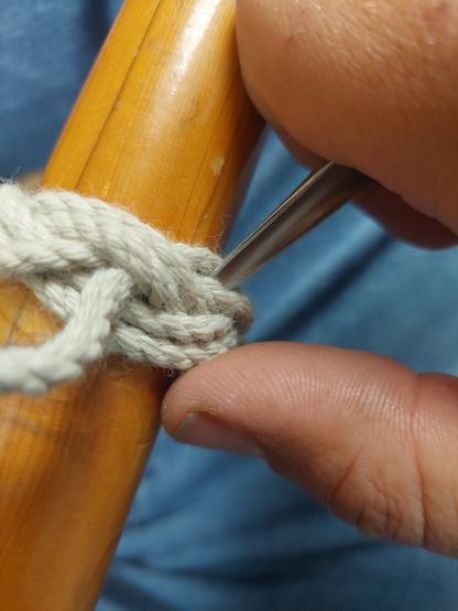 Ein Türkenbund als Handschutz wird um einen Paddel-Griff gebunden. Im Bild ist eine Hand zu sehen, die einen Marlspieker hält, um Bucht für Bucht den Takling nach zu spannen.