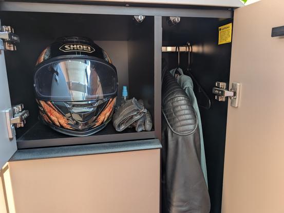 Cubicle closet showing a motorcycle helmet and gloves in one cubby and an armored leather jacket in the closet part.