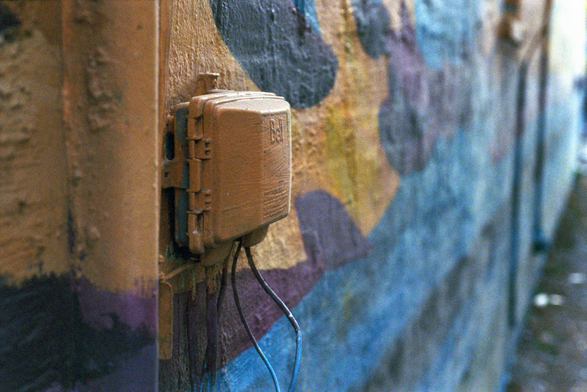 A small Bell Telephone utility box with two wires dangling below it has been painted over as part of a colourful mural of orange, yellow, and blues.