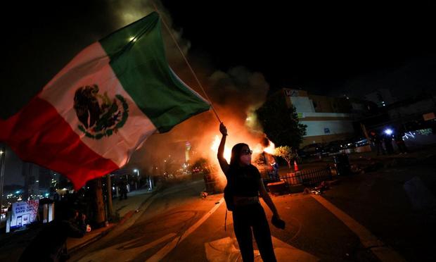 Una manifestante ondea una bandera de México frente a contenedores en llamas, durante una protesta contra las redadas de inmigración en el centro de Los Ángeles, el 8 de junio de 2025. (Aude Guerrucci / Reuters)
