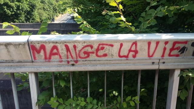 Sur la balustrade d'une passerelle, on a écrit en rouge : MANGE LA VIE