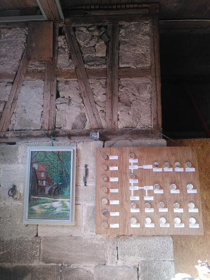 Eine Wand im innren der Mühle. Sie besteht aus Fachwerk. Im unteren Teil hängt eon Gemälde der Mühle und eine Schautafel mit Gläsern, die verschiedene Getreide enthalten in verschiedenen Mahlgraden und Zuständen.