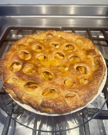 Freshly baked double crust apple pie on a stainless stovetop. The top crust is pierced by numerous circular holes as a decorative motif.