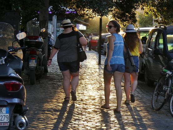 Dominica, Emily and Madeline walking on the sidewalk in downtown Rome, Italy, walking into a sunset with the sun reflecting off of the sidewalk.