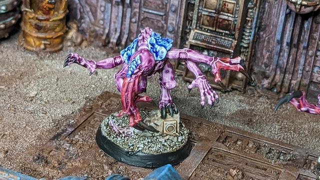A closeup of the other purple blue alien with bloody tentacles and bloody claws.in the rusty background is also a dirty yellow barrel.