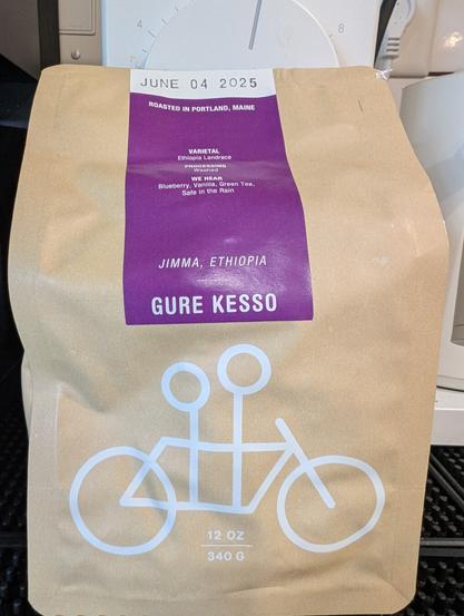 Bag of coffee with a bicycle made out out of basic shapes. Two circle heads representing two people indicating that the bike is a tandem