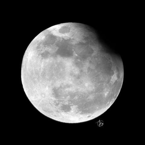 A photograph of Earth's Moon at full phase, except a dark splotch like a bite from a cookie has been taken out of the northeastern limb, caused by a partial lunar eclipse.