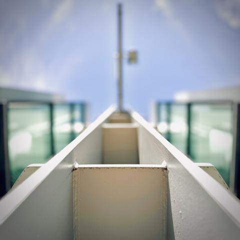 A white steel beam extends up into the partly cloudy midday sky with a large vertical banner attached and viewed only from its thin underside below, while sea-foam green windows flank the banner and beam on each side.