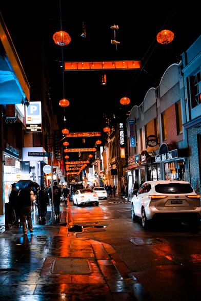 Long view down a red-lantern-lit street in Chinatown, with pedestrians walking down wet sidewalks