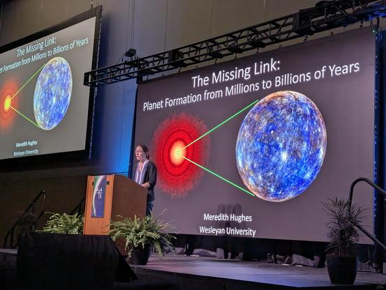 Meredith Hughes stands on stage behind a podium, in front of a large screen.
The slide on screen:
The Missing Link: Planet Formation from Millions to Billions of Years. Meredith Hughes, Wesleyan University