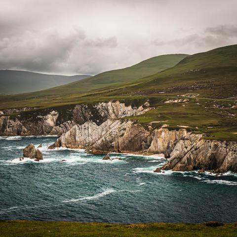 Rugged white sea cliffs on the right with rolling green hills on the left, stormy waters in the foreground, and cloudy skies above.