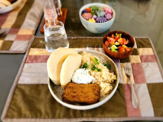 A stone plate with rice, crusted salmon, pita and tzatiki. There is a wooden bowl with a garden salad to the side. It is set on a quilted placemat.

The placemat is green, tan, dusty rose and grey. The colors are arranged in an offset grid. There's a second placemat to the side with the same colors and pattern just in a different combination.