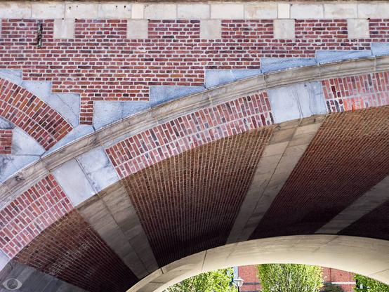 Part of a train underpass with a brick and concrete arch (but mostly bricks.) Lower right a few trees behind it or visible.