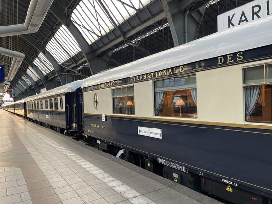 Ein Foto schräg über den Bahnsteig in die Länge auf der man mehrere Orient-Express Wagen am Stück sieht.