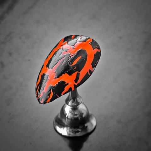 A single artificial nail, mounted on a small chrome stand, dominates the frame with its fierce design. The nail is coated in a searing neon orange polish, partially concealed by a wild web of black crackle lacquer. The cracked black topcoat reveals the glowing orange beneath like lava breaking through volcanic stone—chaotic, raw, and sinfully striking. The grayscale background fades into obscurity, leaving the nail to steal the spotlight with its untamed, post-apocalyptic glam.